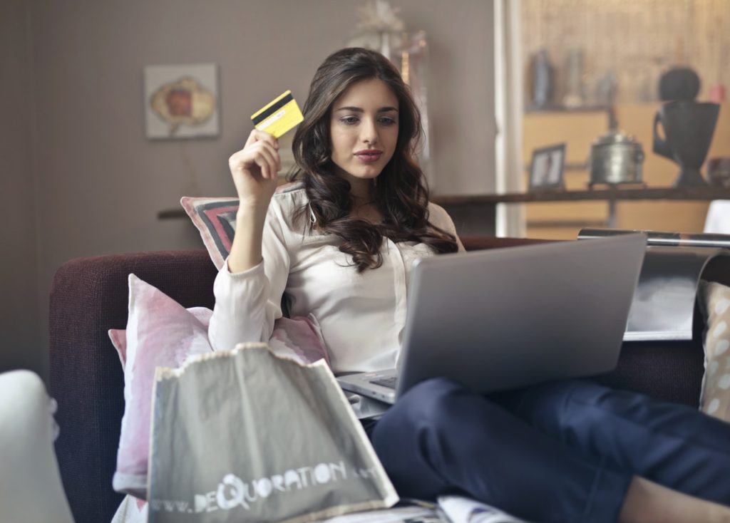 Woman holding up a credit card and thinking about buying a product online