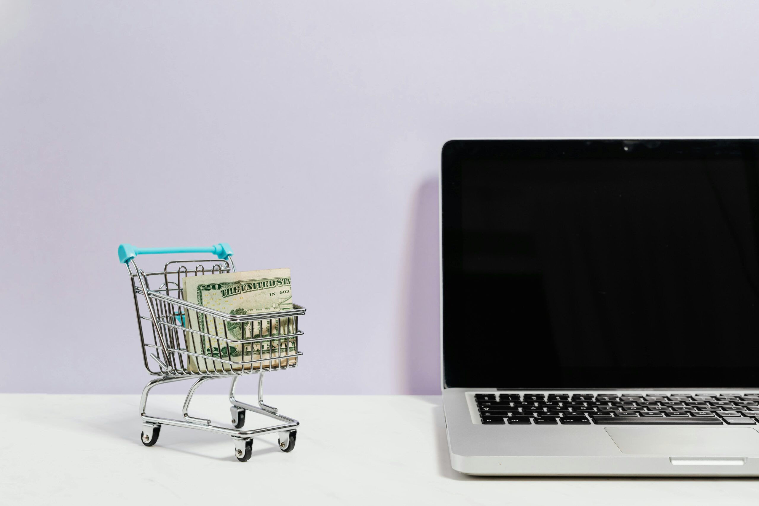 Growth Rocket Macbook Pro on White Table Beside a Miniature Shopping Cart With Money